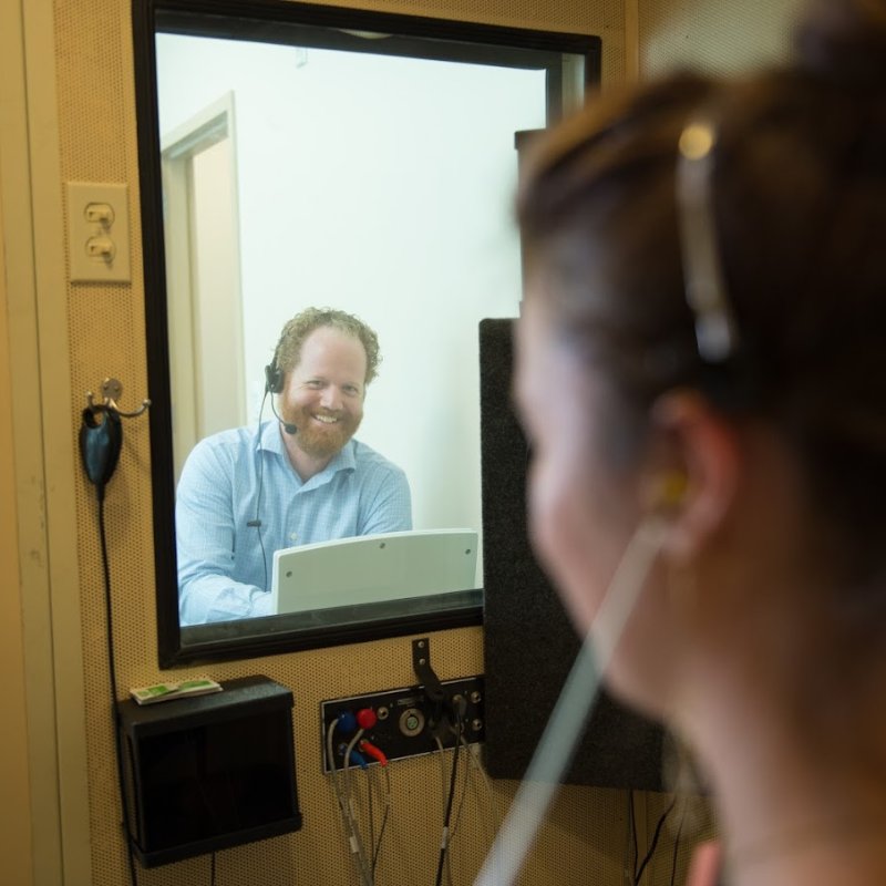 Dr. Gardner smiling through the window of the hearing test sound booth
