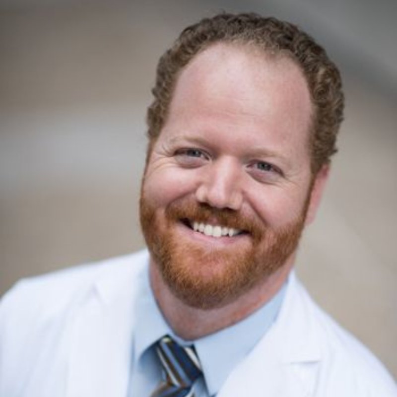 Dr. Robert Gardner, audiologist, smiling in a white coat, light blue shirt and striped tie